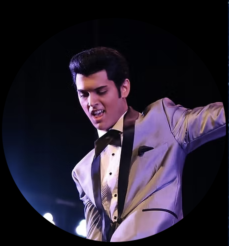 Male performer in a light gray tuxedo and black bow tie mid-dance on stage under bright lights.