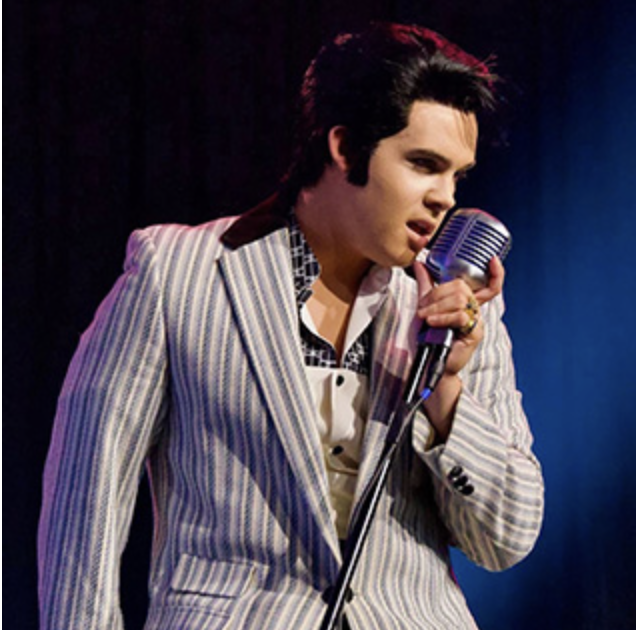 Elvis-like male singer in a light striped suit performing into a retro microphone on stage.