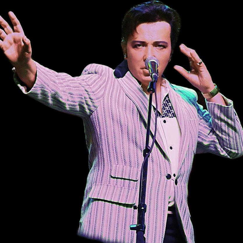 Elvis Presley in a pale striped suit singing into a microphone with an outstretched arm on stage